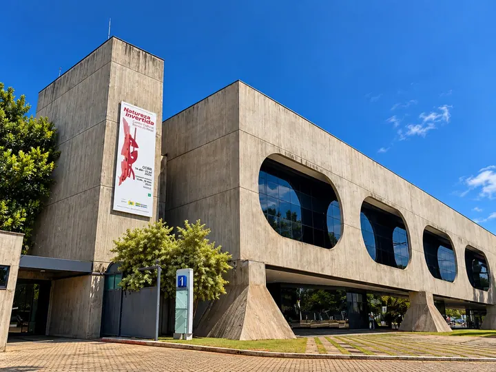 Cartaz “Natureza Inventada” na lateral de concreto do prédio, com as janelas em formato de gota ao fundo